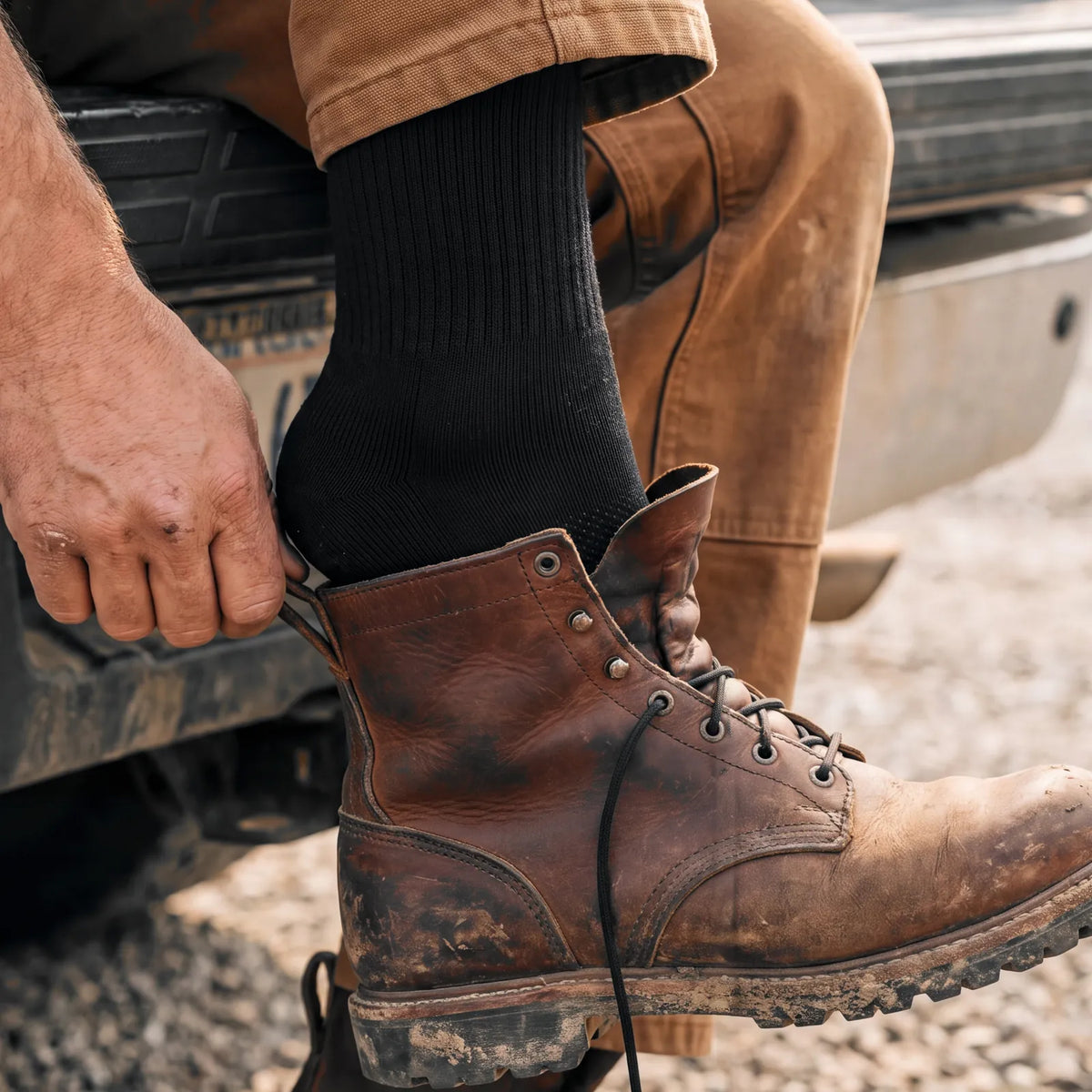 Pulling a leather work boot on over a black Merino Boot Sock at a truck tailgate
